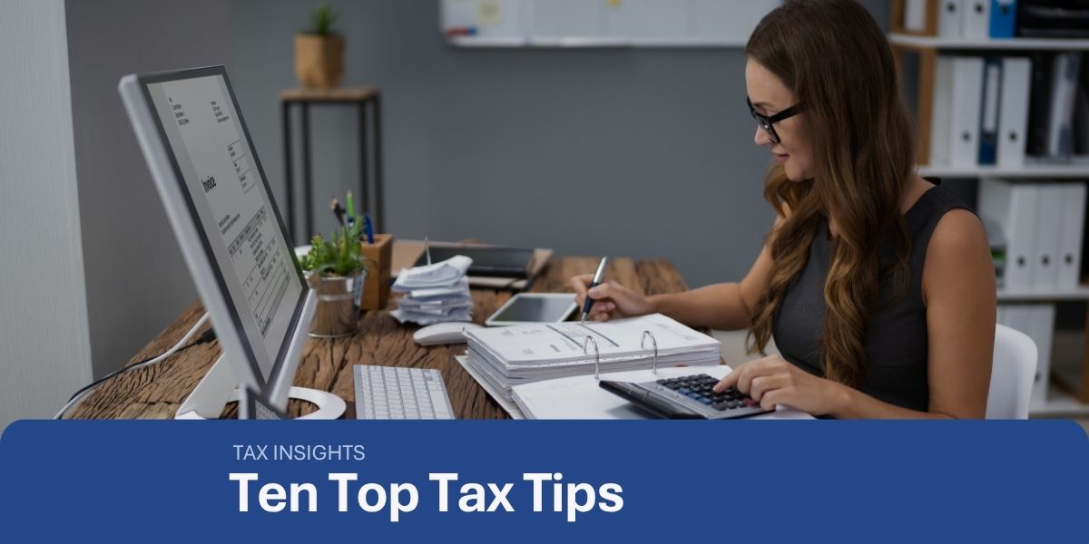 a woman sitting at a desk with a laptop, screen and financial documentsused on a blog about how to reduce tax
